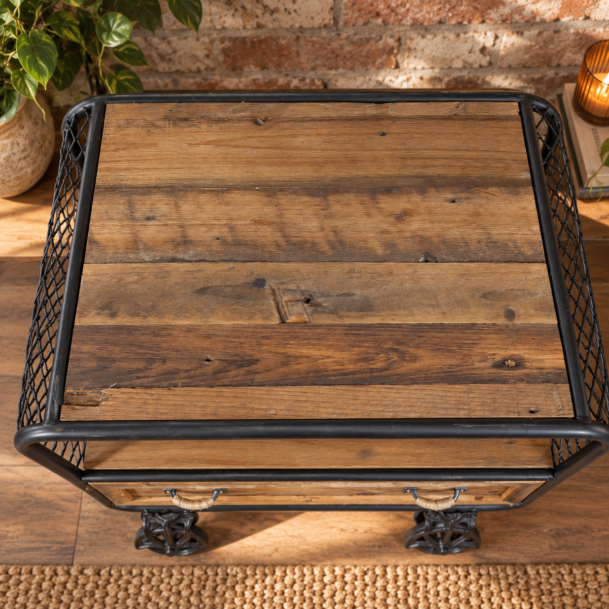 A rustic side table with a weathered brown wooden top, a black metal wire frame, and decorative black metal feet, shown from a top-down angle.